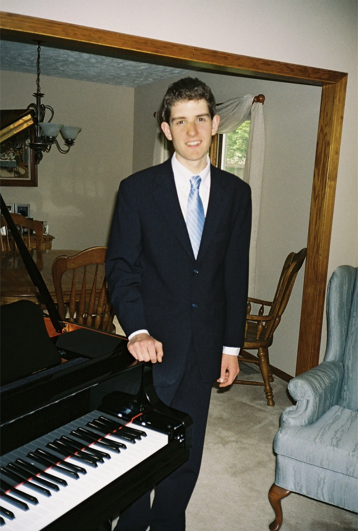 The author as a young man in a navy suit, standing with one hand resting on a grand piano